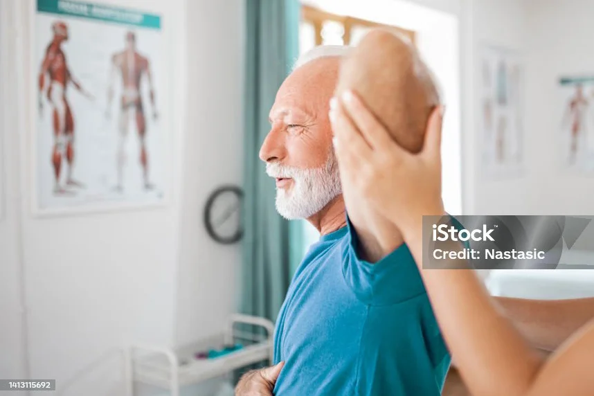 Physiotherapeutin bewegt den Arm eines älteren Patienten in einem hellen Behandlungsraum